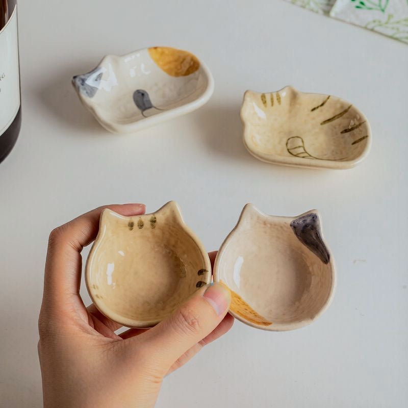 Two cat-shaped ceramic dipping dishes in cream and beige, shown side by side.