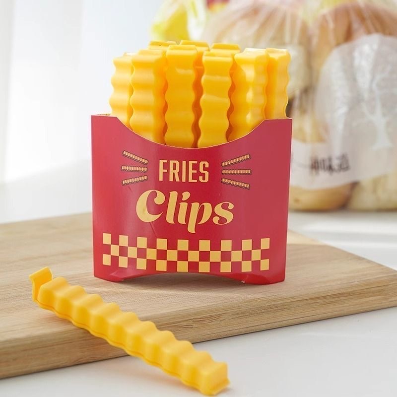Red fries-shaped storage holder filled with yellow wavy food bag clips, with one clip displayed on a wooden board.