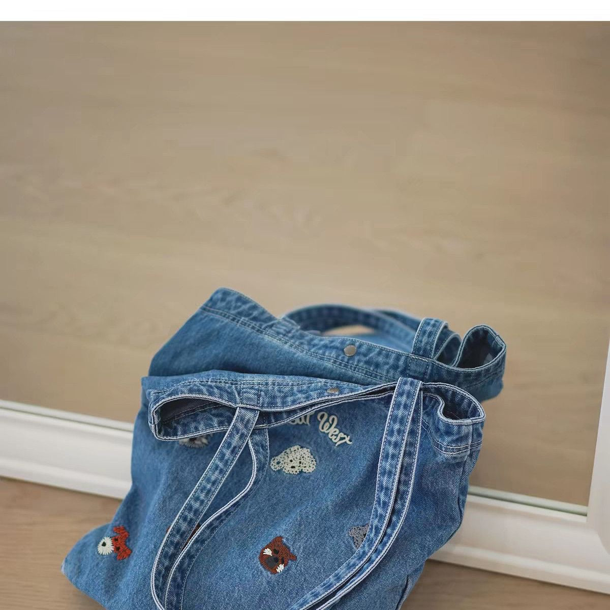 Folded washed-blue denim tote showing embroidered animal motifs and handles