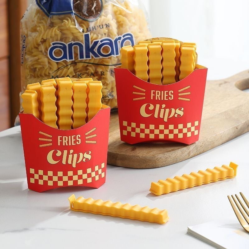 Yellow food bag clips displayed in the red fries-shaped holder beside pantry groceries on a kitchen counter.