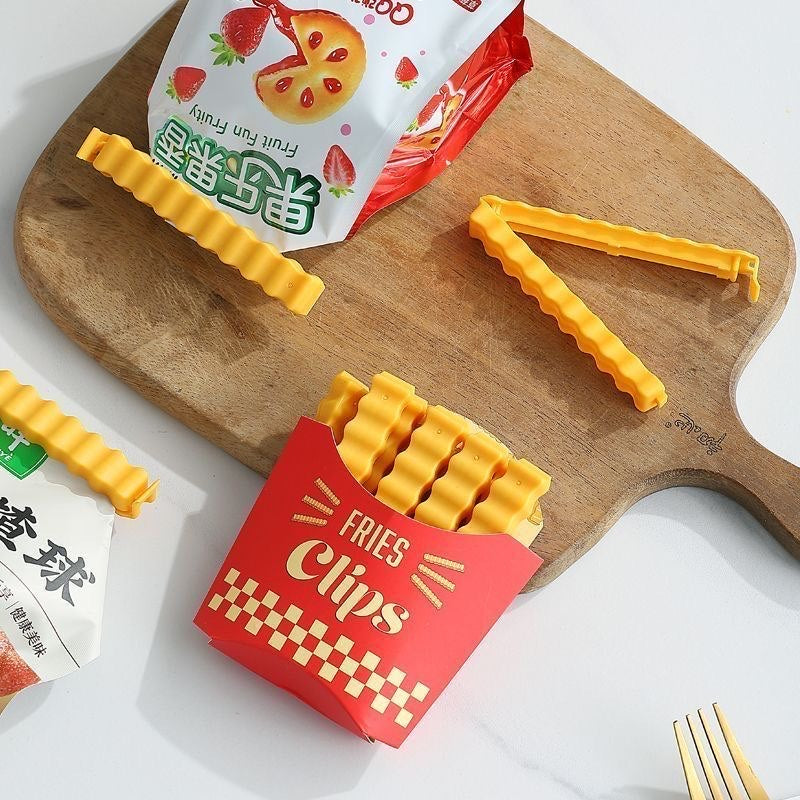 Yellow wavy food bag clips and the red fries-shaped storage holder arranged on a cutting board.
