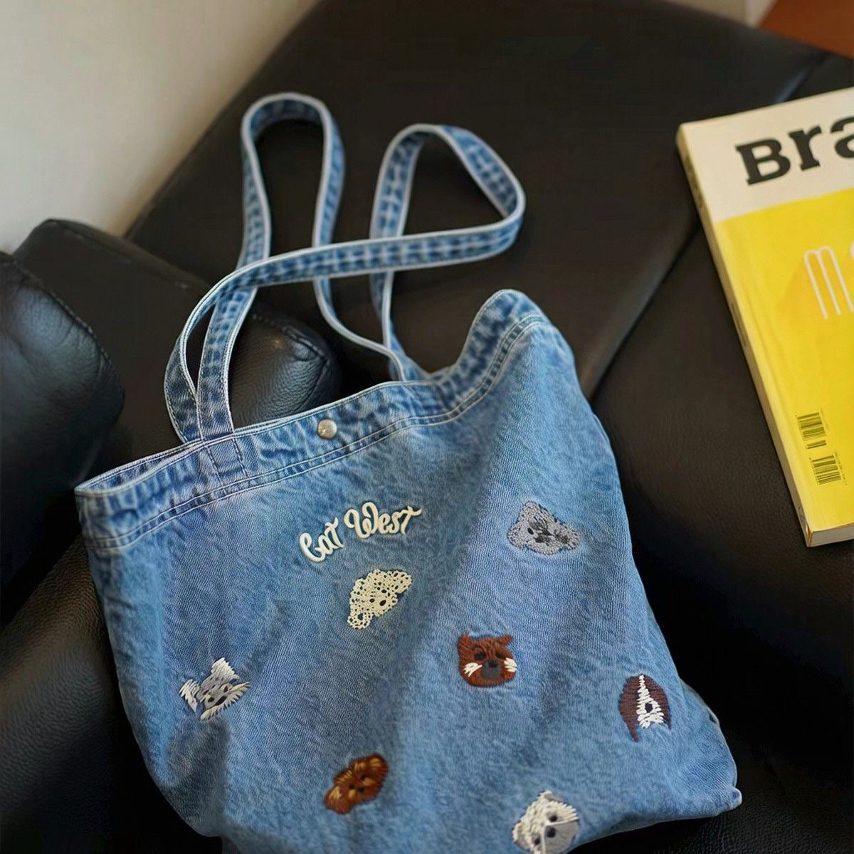Washed-blue denim tote with embroidered animal motifs styled beside a book